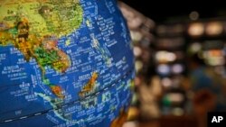Para pelanggan membaca buku dekat sebuah bola Dunia yang menunjukkan negara-negara Asia Tenggara di Laut China Selatan dengan ‘sembilan garis putus-putus (Nine-dash line)’ yang diklaim sebagai wilayah China, di sebuah toko buku di Beijing, 13 Juli 2018. (Foto: AP)

