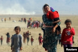FILE - Displaced Yazidis, fleeing violence from forces loyal to the Islamic State group, head toward the Syrian border, Aug. 11, 2014.