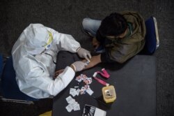 Seorang petugas kesehatan (kiri) mengambil sampel darah dari seorang pengendara motor yang melanggar Pembatasan Sosial Berskala Besar (PSBB) di sebuah kantor polisi di Surabaya, 3 Mei 2020. (Foto: AFP)