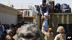 美国陆军发布的照片显示，在喀布尔哈米德·卡尔扎伊国际机场，一名阿富汗男子把他的孩子交给英军伞兵，美国陆军82空降师成员在旁执行安全警戒。(2021年8月26日)