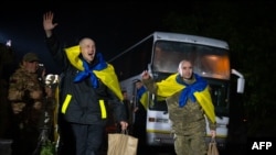 身披蓝黄色乌克兰国旗的战俘步下巴士，热烈期待与亲人团聚。(乌克兰总统新闻处提供)