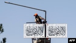 An Afghan worker hangs a Taliban flag along a street in Kabul on Aug. 13, 2023.