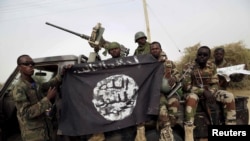 FILE PHOTO - Nigerian soldiers hold up a Boko Haram flag that they had seized in the recently retaken town of Damasak, Nigeria.