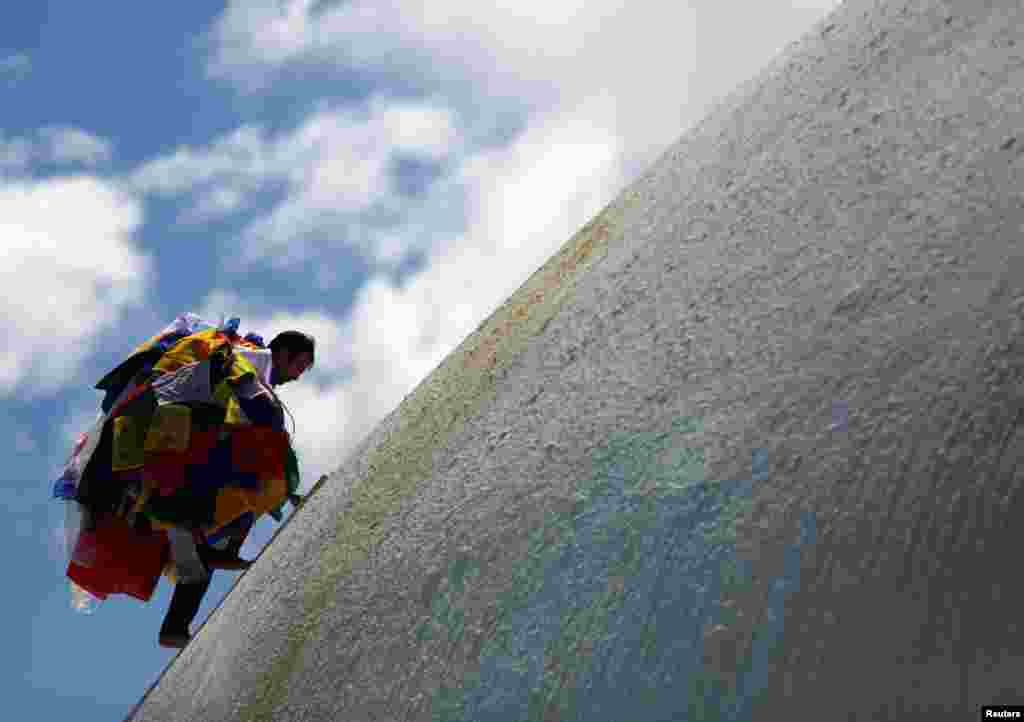 A man carrying prayer flags offered by devotees climbs to hang them along the Boudhanath Stupa, a UNESCO world heritage site famous among tourists, in Kathmandu, Nepal.