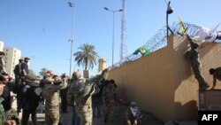 Pripadnici proiranske Hašid al Šabi paramilitarne grupe u Iraju kače zastavu na bodljikavu žicu na spoljnom zidu Ambasade SAD u Bagdadu, tokom nasilnih demonstracija, 31. decembra 2019.