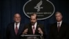 Human Services Secretary Alex Azar speaks as Centers for Disease Control and Prevention (CDC) director, Robert R. Redfield, left, and Deputy Secretary of State Stephen Biegun listen during a press conference, Feb. 7, 2020 in Washington.