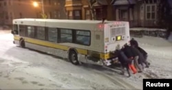 People push a bus on an icy road in Boston, in this still image taken from a Jan. 4, 2018, social media video. Karen Lyons Clauson/via Reuters