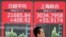 A man walks past an electric screen showing Japan's Nikkei and Shanghai Stock Exchange markets' indices outside a brokerage in Tokyo, July 1, 2019.