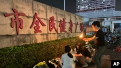 Seorang perempuan menyalakan lilin sebagai persembahan di luar "Zhuhai People's Fitness Plaza" di Zhuhai, provinsi Guangdong, China selatan, tempat seorang pria menabrakkan mobilnya ke orang-orang yang sedang berolahraga di pusat olahraga itu, 12 November 2024. (Ng Han Guan/AP)