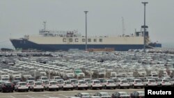 FILE - Newly-manufactured cars and a container ship are seen at Dayaowan port of Dalian, Liaoning province, June 10, 2012. 