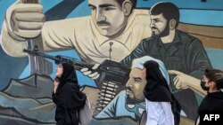 Beberapa perempuan berjalan melewati mural anti-Israel yang menggambarkan pejuang dengan senapan serbu di sepanjang dinding di Alun-Alun Palestina di Tehran pada 14 April 2024. (Foto: AFP)