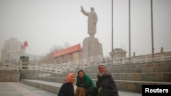 Warga etnis Uighur duduk-duduk dekat patung mendiang Ketua Mao Zedong di Kashgar, Wilayah Autonomi Xinjiang Uighur, China, 23 Maret 2017.
