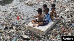 Anak-anak sebuah daerah kumuh di Jakarta duduk di atas rakit buatan di sungai yang dipenuhi sampah. (Foto: Dok)
