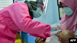 Seorang petugas medis mengenakan baju pelindung memberikan vaksinasi kepada seorang bayi di sebuah puskesmas di Banda Aceh, 18 Mei 2020. (Foto: AFP)