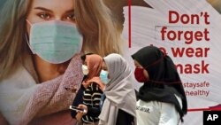 Perempuan mengenakan masker melewati poster promosi kesadaran pandemi Covid-19 di sebuah pusat perbelanjaan di Jakarta, 1 Juli 2020. (Foto: dok).