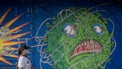 Seorang perempuan mengenakan masker pelindung berjalan melewati mural bertema virus corona saat wabah COVID-19 terus berlanjut di Solo, Jawa Tengah, 21 Februari 2021. (Foto: Antara/Mohammad Ayudha via Reuters)