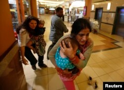 Women carrying children run for safety as armed police hunt gunmen who went on a shooting spree in Westgate shopping center in Nairobi, Sept. 21, 2013.