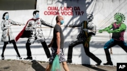 Seorang pria mengenakan masker, berjalan melewati dinding mural yang menggambarkan tarik-menarik soal virus corona antara pekerja kesehatan dan Presiden Brasil Jair Bolsonaro, di Sao Paulo, Brasil, 19 Juni 2020. (Foto: dok).