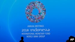Para pekerja melewati spanduk pertemuan tahunan IMF-Bank Dunia yang dipasang di ruang konferensi di Bali, 8 Oktober 2018. 
