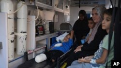 Seorang anak Palestina yang kakinya diamputasi duduk di dalam ambulans bersama kerabatnya saat menunggu untuk dikirim keluar dari Jalur Gaza untuk mendapatkan pengobatan. Pengiriman pasien tersebut berlangsung di Khan Younis, pada 27 Juni 2024. (Foto: AP/Abdel Kareem Hana)