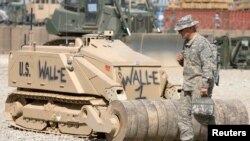 Một binh sĩ Mỹ đi ngang qua con robot dọn mìn được đặt theo tên một nhân vật họat hình "Wall-E" tại trại Leatherneck ở tỉnh Helmand, miền nam Afghanistan, 10/3/2010. REUTERS/Shamil Zhumatov