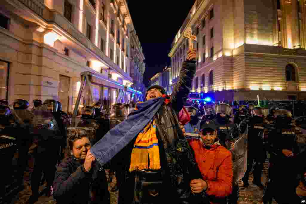 A woman screams holding a cross in front of riot policemen blocking a street following clashes with supporters of Calin Georgescu after Romania's electoral body rejected his candidacy in the presidential election rerun in Bucharest.