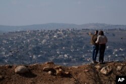 An Israeli couple observe the damaged buildings of a village in southern Lebanon as they stand near the Israeli-Lebanese border, during the ceasefire between Israel and Hezbollah, on Nov. 30, 2024.