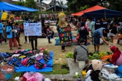 Aktivis berpakaian tradisional membawa plakat untuk sosialisasi vaksinasi COVID-19 di sebuah pasar di Pekanbaru, Riau, 1 April 2021. (Foto: Wahyudi / AFP)