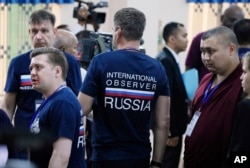 Sejumlah pengamat pemilu internasional dari Rusia mengamati jalannya pemungutan suara di sebuah TPS di Takhmua, Provinsi Kandal, di tenggara Phnom Penh, Ibu Kota Kamboja, Minggu, 23 Juli 2023. (Foto: Heng Sinith/AP Photo)