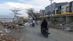 Warga melintas dengan sepeda motor di antara puing-puing dari bekas bangunan yang rusak akibat gempa bumi dan terjangan tsunami di pantai teluk Palu (24/11) Foto: VOA/Yoanes Litha