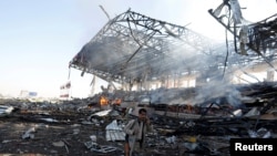 Seorang pejuang Houthi sambil berbicara di ponselnya, berjalan melewati lokasi yang baru dihantam oleh serangan udara koalisi pimpinan Saudi, di Sana'a, Yaman, Minggu (5/11). 