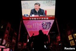 2024년 12월 9일 중국 베이징에서 한 남성이 시진핑 중국 국가주석이 공산당 정치국 회의에 참석한 뉴스 영상을 보여주는 대형 스크린 앞을 스쿠터를 타고 지나가고 있다.