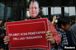 Seorang pria bertopeng bergambar Firli Bahuri, Ketua Komisi Pemberantasan Korupsi (KPK), membawa plakat bertuliskan "Selamat atas penetapan Firli sebagai tersangka" saat melakukan aksi di luar gedung KPK di Jakarta, 23 November 2023. (Foto: REUTERS/Ajeng Dinar Ulfiana)