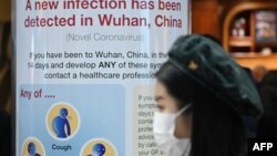 Seorang perempuan mengenakan masker melintas di depan papan pemberitahuan Kesehatan Masyarakat Inggris di Terminal 4 Bandara Heathrow di London. (Foto: AFP)