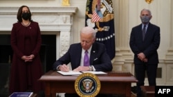 FILE - U.S. President Joe Biden signs executive orders as part of the COVID-19 response as U.S. Vice President Kamala Harris, left, and Director of NIAID Anthony Fauci look on in the State Dining Room of the White House in Washington, Jan. 21, 2021.
