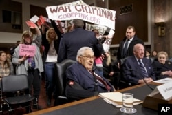 基辛格（左）和舒尔茨与奥尔布赖特三位前国务卿在参议院军事委员会作证时，抗议者干扰会场。（2015年1月29日）