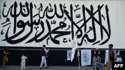 A vendor selling Taliban flags waits for customers next to a large Taliban flag in Kabul on Sept. 24, 2021. 