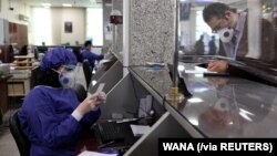 Seorang karyawan bank dengan mengenakan pelindung wajah melayani nasabah di tengah pandemi virus corona (Covid-19) di Teheran, Iran, 17 Maret 2020. (Foto: Ali Khara West Asia News Agency via Reuters)