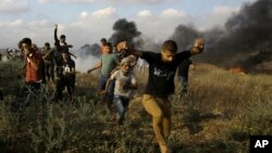Palestinian protesters take cover from tear gas fired by Israeli troops as others burn tires near the Gaza Strip's border with Israel, during a protest east of Khan Younis, in the Gaza Strip, June 1, 2018.