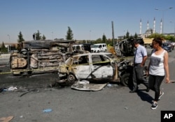 FILE - Turkish citizens walk past burnt and destroyed police and civilian vehicles near the presidential palace, in Ankara, Turkey, July 17, 2016, that were attacked by a Turkish airstrike during a military coup late Friday.