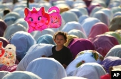 FILE - A Muslim girl holds a balloon during a morning prayer marking the Eid al-Adha holiday on a street in Jakarta, Indonesia.
