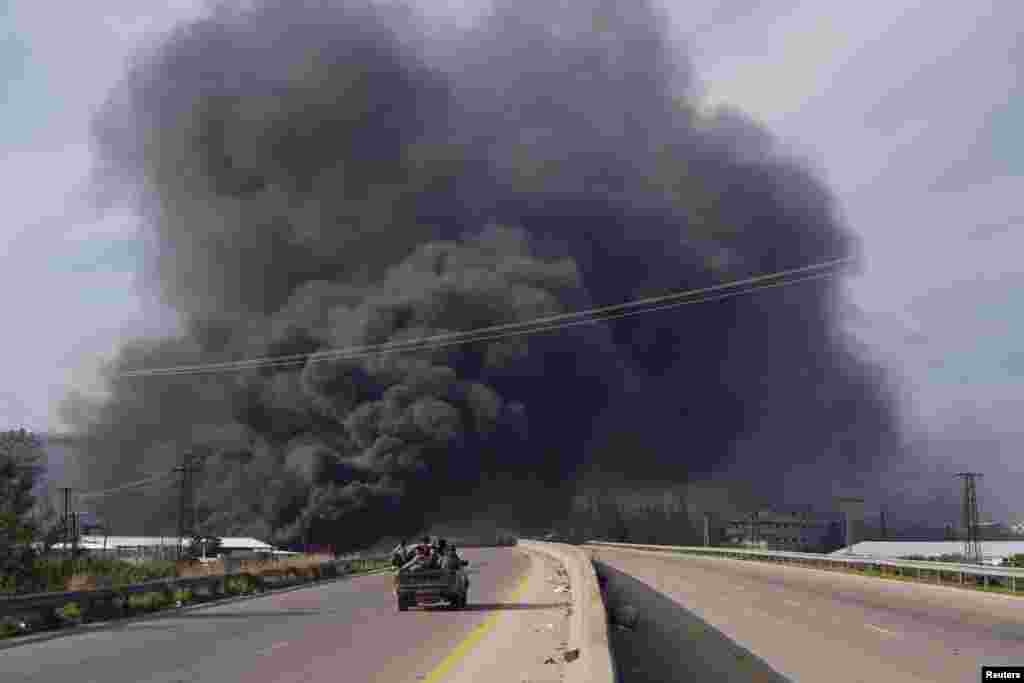 Smoke rises while members of the Syrian forces ride on a vehicle as they battle against a nascent insurgency by fighters from ousted leader Bashar al-Assad&#39;s Alawite sect, in Latakia, Syria.