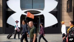 Seorang pemandu wisata China memimpin sekelompok wisatawan melewati toko pengecer pakaian olahraga asal Amerika, Under Armour, di sebuah kawasan perbelanjaan di Beijing, Selasa 25 September 2018 (foto: AP Photo/Mark Schiefelbein)