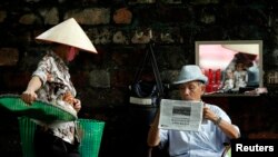 រូបឯកសារ៖ ស្ត្រី​ម្នាក់​កណ្ដៀត​ចង្អេរ​មួយ​ដើរ​ជិត​បុរស​ម្នាក់​ ដែល​កំពុង​អង្គុយ​អាន​កាសែត​ ថ្ងៃ​ទី១៣ ខែកញ្ញា ឆ្នាំ២០១៣។