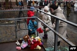 A local resident and children lay flowers at the site where a helicopter crashed near a kindergarten in Brovary, outside the capital Kyiv, Jan. 18, 2023