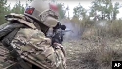 In this handout photo released by Russian Defense Ministry Press Service on Oct. 19, 2022, a Russian Army soldier fires a sniper rifle at an unspecified location in Ukraine.