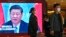 A security personnel checks a journalist near a TV screen showing image of President Xi Jinping at a media hotel in Beijing, Oct. 21, 2022.