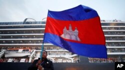 FILE - A Cambodian man holds his national flag in front of the MS Westerdam, owned by Holland America Line, dockked at the port of Sihanoukville, Cambodia, Friday, Feb. 14, 2020.