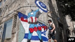 Seorang pria berjalan melewati mural yang menggambarkan Presiden AS Joe Biden berpakaian karakter komik Marvel "Captain America" berdiri di depan bendera Israel dan mengangkat perisai bergambar simbol Bintang Daud, di pinggir jalan kota Tel Aviv. (AFP) 