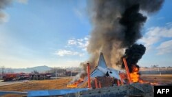 Api dan asap tampak mengepul dari bagian ekor pesawat Jeju Air Boeing 737-800 setelah pesawat tersebut jatuh saat berusaha mendarat di Bandara Internasional Muan di provinsi Jeolla Selatan, pada 29 Desember 2024. (Foto: Yonhap/AFP)